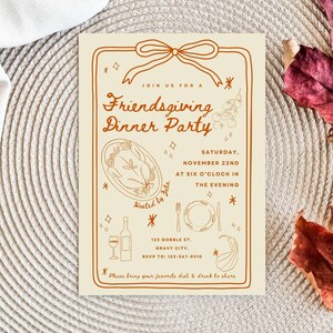 Puede incluir: Invitaci&oacute;n a una cena de Acci&oacute;n de Gracias entre amigos. La tarjeta beige presenta ilustraciones marrones de un pavo, vino y una mesa. El texto incluye la fecha, la hora y el lugar. La invitaci&oacute;n est&aacute; decorada con un lazo y hojas de oto&ntilde;o.