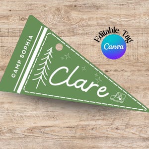 May include: A green pennant-shaped tag with the name "Clare" in white script. The tag includes a tree graphic, stars, and the text "Camp Sophia." A Canva tag is in the upper right corner. The tag is on a wood grain surface.