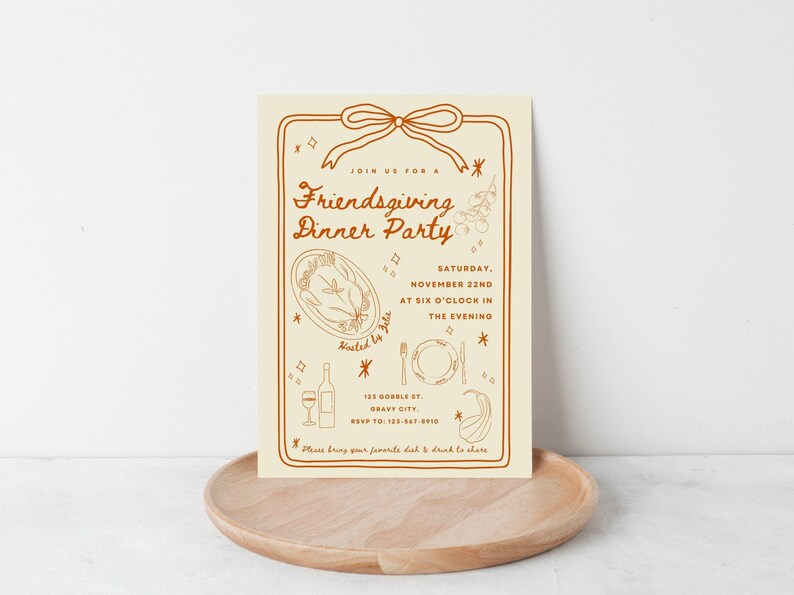 Puede incluir: Una invitaci&oacute;n crema para una fiesta de Friendsgiving con texto e ilustraciones marrones. La invitaci&oacute;n incluye la fecha, la hora y el lugar. La invitaci&oacute;n est&aacute; sobre una bandeja de madera.