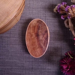 Può includere: Un vassoio da portata ovale in legno con venature di legno marrone scuro. Il vassoio è su una superficie grigia testurizzata.