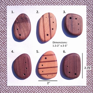 Peut inclure: Six boutons en bois lisses en forme de galet numérotés de 1 à 6. Certains sont en bois brun foncé uni, d'autres présentent des rayures de bois clair et foncé. Chaque bouton a de petits trous. Le texte indique des dimensions de 3,8-5 cm par 5-7,6 cm.