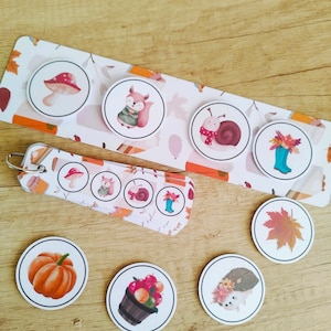 Könnte beinhalten: Eine Sammlung runder Aufkleber und ein Schlüsselanhänger mit herbstlichen Illustrationen. Designs umfassen einen Pilz, ein Eichhörnchen, eine Schnecke, Blumen in einem Stiefel, einen Kürbis, einen Obstkorb, ein Blatt und einen Igel.