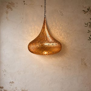 May include: A teardrop-shaped pendant light fixture crafted from metallic gold-toned material. The surface features intricate, laser-cut geometric patterns that allow light to project outward, creating a detailed shadow effect on the wall.