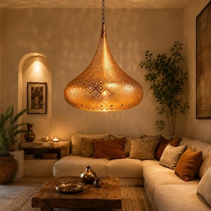 May include: A large, teardrop-shaped pendant light fixture made of metallic gold-toned material, featuring intricate laser-cut geometric patterns that allow light to pass through, suspended from the ceiling by a thin metal chain.