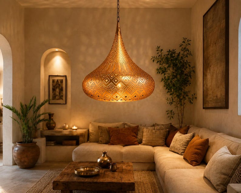 May include: A large, teardrop-shaped pendant light fixture made of metallic gold-toned material, featuring intricate laser-cut geometric patterns that allow light to pass through, suspended from the ceiling by a thin metal chain.