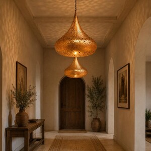 May include: Two tiered, teardrop-shaped pendant lights made of metallic gold-toned material with intricate, perforated geometric patterns that cast detailed shadows on the surrounding walls and ceiling in a hallway setting.