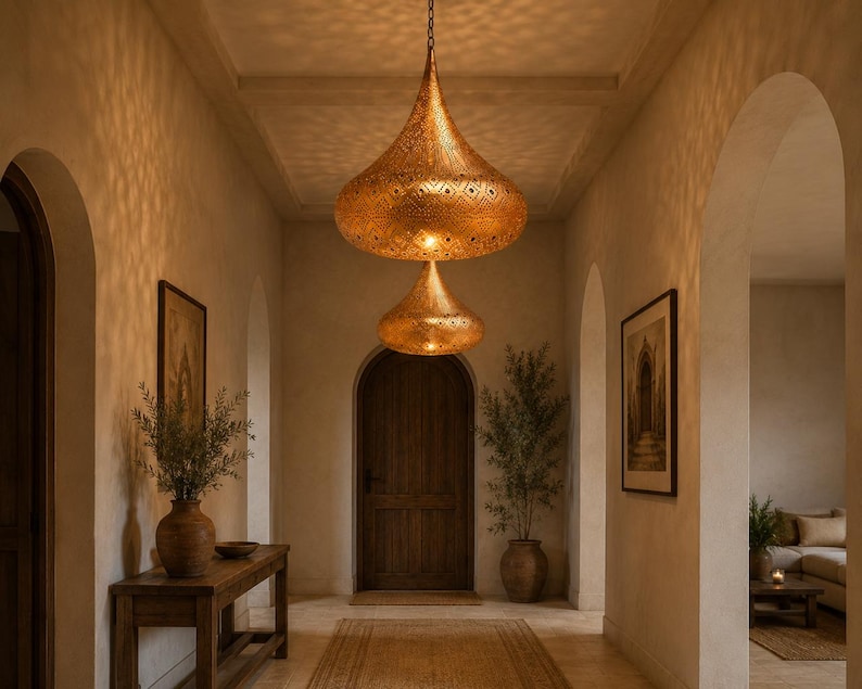 May include: Two tiered, teardrop-shaped pendant lights made of metallic gold-toned material with intricate, perforated geometric patterns that cast detailed shadows on the surrounding walls and ceiling in a hallway setting.