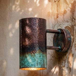 Peut inclure: Une applique murale cylindrique avec une texture en cuivre martelé. La partie supérieure présente une finition brun métallique chaude, tandis que la section inférieure passe à une patine sarcelle oxydée vibrante. Fixée par deux bras.