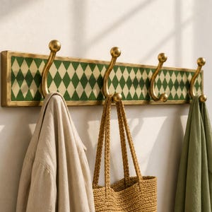 Peut inclure: Un porte-manteau mural composé d'un cadre rectangulaire avec une incrustation à motif de losanges verts et crème. Il comprend quatre crochets en métal doré avec des extrémités en forme de boule. Un vêtement beige, un sac en paille et un tissu vert y sont suspendus.