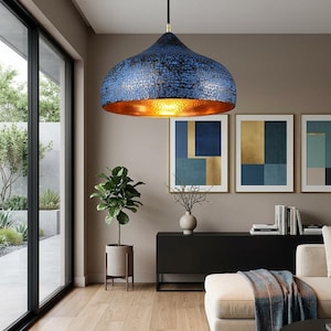 May include: A blue and gold pendant light fixture with a textured surface hangs from the ceiling. The interior of the light is gold, and the fixture is suspended above a living room with artwork and a sofa.