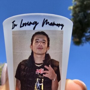 May include: A white shot glass with a photo of a person and the text "In Loving Memory Joseph M. Cuv 02.08.2000-10.28.2020"