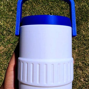 May include: A white cylindrical container with a textured middle band and a solid blue lid featuring an integrated arched handle. The container has a smooth finish and a distinct horizontal ridge separating the upper and lower sections of the body.