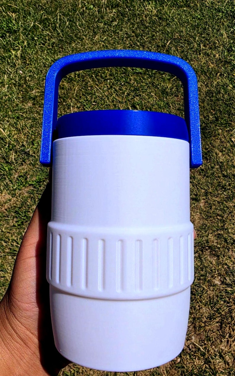 May include: A white cylindrical container with a textured middle band and a solid blue lid featuring an integrated arched handle. The container has a smooth finish and a distinct horizontal ridge separating the upper and lower sections of the body.
