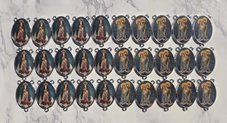 May include: A collection of twenty-seven oval metal charms arranged in three rows. The charms feature two alternating religious images: one depicting a crowned figure in robes and another showing a group of three figures with halos in blue tones.