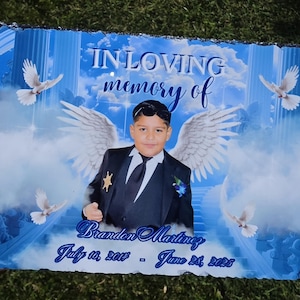 May include: A rectangular slate memorial plaque featuring a printed image of a child in a suit with angel wings, surrounded by white doves and blue clouds. The text reads IN LOVING memory of Brandon Martinez July 16, 2014 - June 28, 2025.