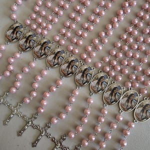 May include: A collection of rosaries featuring light pink pearl beads and silver-toned metal chains. Each rosary includes an oval-shaped pendant containing a photographic portrait of a person and a silver-toned crucifix at the bottom end.