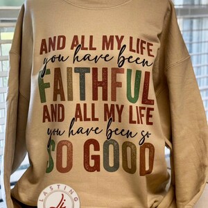 Könnte beinhalten: Beiges Sweatshirt mit dem Text "AND ALL MY LIFE you have been FAITHFUL AND ALL MY LIFE you have been so SO GOOD" in verschiedenen Farben. Das Kleidungsstück hat einen Rundhalsausschnitt und lange Ärmel. Das Markenlogo ist sichtbar.