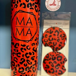 May include: A red and black tumbler with a leopard print design. The tumbler has the word "MAMA" printed on it in black. The tumbler is accompanied by two matching coasters.