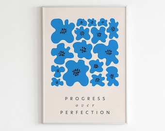 May include: A framed print with a light beige background and blue abstract flowers. The text "PROGRESS over PERFECTION" is printed below the flowers. The text "LETTERS TO FUTURE self" is printed below the frame.