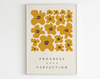 May include: A framed print with a white background and a design of yellow abstract flowers with black centers. The text "PROGRESS over PERFECTION" is printed below the flowers. The text "LETTERS TO FUTURE self" is printed below the frame.