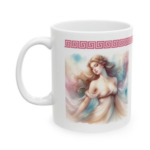 May include: White ceramic mug with a colorful illustration of a woman with long blonde hair wearing a white dress. The image is surrounded by a red Greek key border.