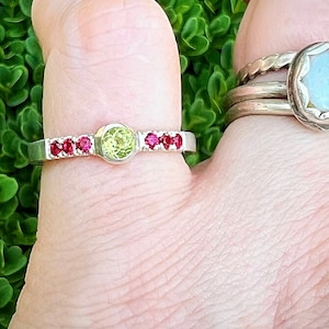 May include: A silver ring with a green gemstone and red gemstones on the band.