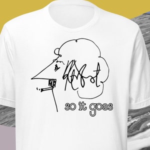 May include: White t-shirt featuring a black line drawing of a profile with a large nose and curly hair. The text "so it goes" is printed below the drawing in a simple font. The shirt is made of a soft material.