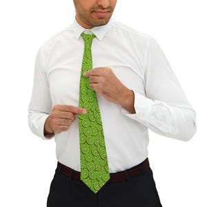 May include: A green tie with a repeating pattern of kiwi fruit slices. The tie is a vibrant green color with brown and green details. The tie is being adjusted by a person wearing a white dress shirt.