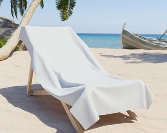 May include: A white beach towel draped over a wooden deckchair on a sandy beach. The chair faces the sea, with a boat in the background. Palm trees and a blue sky complete the scene.
