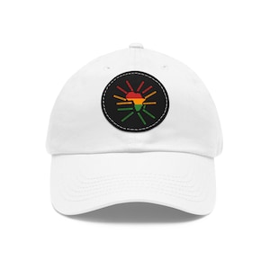 Puede incluir: Gorra de béisbol blanca con un parche circular negro y blanco que presenta un contorno rojo, amarillo y verde del continente africano con líneas radiantes.