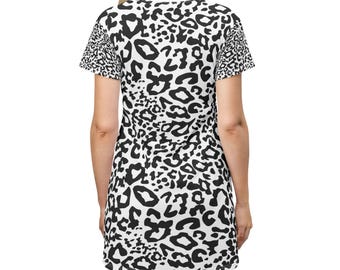 May include: A white t-shirt dress with a black leopard print pattern. The dress has short sleeves and a crew neck. The leopard print covers the entire dress, including the sleeves.