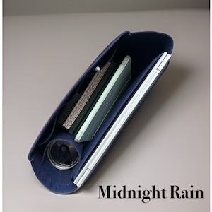 May include: A navy blue felt bag with a zipper closure. The bag is open and shows a laptop, a notebook, and a pen inside. The bag is labeled "Midnight Rain".