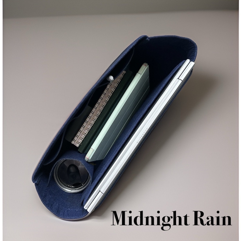 May include: A navy blue felt bag with a zipper closure. The bag is open and shows a laptop, a notebook, and a pen inside. The bag is labeled "Midnight Rain".