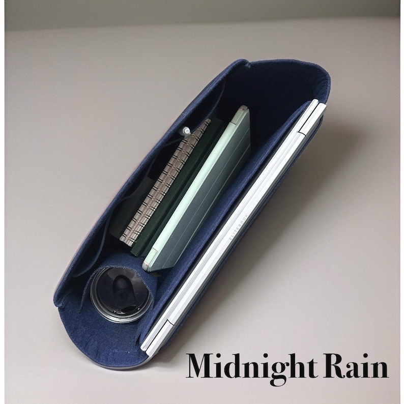 May include: A navy blue felt tote bag with a zipper closure. The bag is open and filled with a notebook, a tablet, and a phone. The bag is labeled "Midnight Rain".