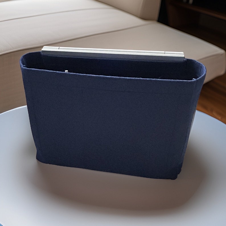 May include: A dark blue felt bag insert for a handbag. The insert has a rigid top and is designed to help organize a handbag.