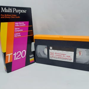 May include: A black Gemini T120 VHS video cassette with an orange top edge and a white label featuring handwritten text: Host: Alice Cooper, MTV - October 21, 1989, 2 Hours with Commercials. Beside it stands the original black, yellow, and pink box.