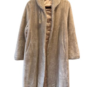 May include: A long, beige faux fur coat with a hood and a drawstring closure. The coat has a satin lining with a floral pattern.