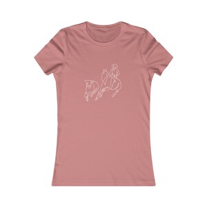 May include: A pink women's t-shirt with a white line drawing of a cowboy riding a horse and herding a cow.