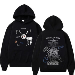 Peut inclure: Sweat-shirt à capuche noir avec un dessin blanc d'un chien sur le devant et une liste de titres de chansons au dos. Le texte au dos indique "For All The Dogs" et comprend des titres de chansons comme "Virginia Beach", "Amen", "Calling For You" et "Fear Of Heights".