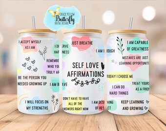 Op de afbeelding: Drie witte bekers met bamboe deksels en rietjes. Elke beker heeft kleurrijke abstracte vormen en positieve affirmaties, zoals "Ik accepteer mezelf zoals ik ben", "Ik ben in staat tot grootsheid" en "Zelfliefde-affirmaties".