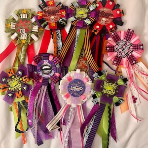 May include: A collection of eight decorative ribbon badges featuring various Halloween-themed designs, text, and patterns. Each badge is crafted with layered ribbons in colors including purple, green, orange, black, and pink, accented with small embellishments.