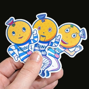 May include: Three cartoon orange stickers with blue and white striped shirts and hats. Each sticker has a different facial expression and a different design on their shirt.