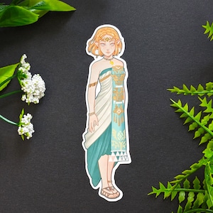 May include: A sticker featuring a cartoon illustration of a woman with blonde hair, wearing a white and blue dress with gold accents. The woman has a crown on her head and is standing with her arms at her sides.