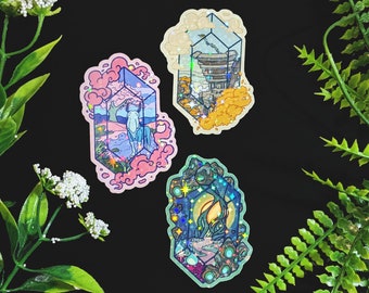 Op de afbeelding: Drie holografische stickers met een kristalprisma-ontwerp. Elke sticker heeft een andere scène in het prisma: een wit paard in een roze en blauwe landschap, een gebouw in een geel en oranje landschap en een bos scène in een blauw en groen landschap.