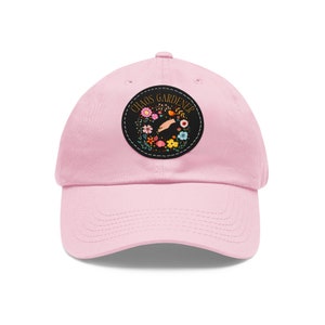May include: Pink baseball cap with a black embroidered patch that says "Chaos Gardener" with a hand holding a flower and a floral wreath around it.