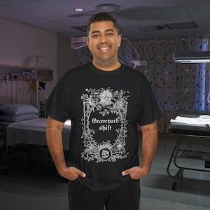 Könnte beinhalten: Schwarzes T-Shirt mit einem weißen Grafikdesign aus einem Totenkopf und einem floralen Rahmen. Der Text "Graveyard Shift" ist in Weiß innerhalb des Rahmens gedruckt.