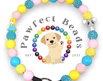 May include: A colorful beaded dog collar with a princess charm, a mouse charm, and a black buckle. The collar is made with yellow, pink, blue, and clear beads. The beads are interspersed with sparkly beads. The collar is surrounded by a rainbow of beads and the text "Pawfect Beads Est. 2023".