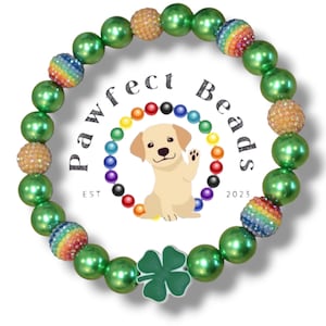May include: Green and gold beaded bracelet with a shamrock charm. The beads are iridescent and have a rainbow design. The bracelet has the text "Pawfect Beads Est 2023" on it.