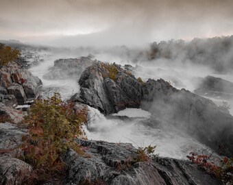 Puede incluir: Un paisaje brumoso y gris con un lecho de río rocoso y una cascada. El agua fluye sobre las rocas y crea una niebla blanca. Las rocas están cubiertas de musgo y líquenes. El cielo es de un gris claro.