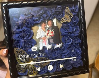 Könnte beinhalten: Ein schwarzer Bilderrahmen mit einem blauen und goldenen Schmetterlingsdesign. Der Rahmen enthält ein Foto von zwei Personen und eine Musikplayer-Oberfläche mit dem Text "Dear Mama" und "2Pac".
